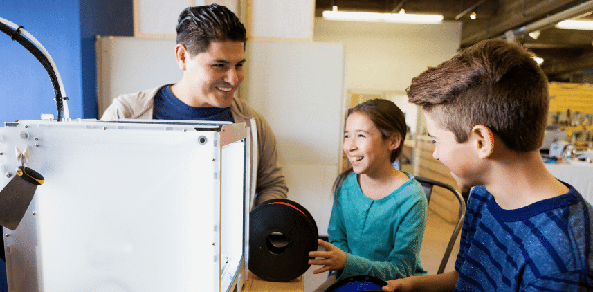 Homme souriant et deux enfants réunis autour d'une imprimante 3D