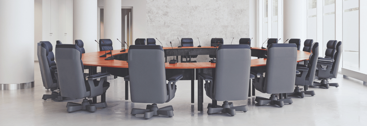 an empty boardroom with white concrete walls. a circular empty desk in the center, with 20+ empty computer chairs. 