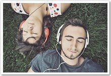 A couple lying in the grass listening to music with headphones on.