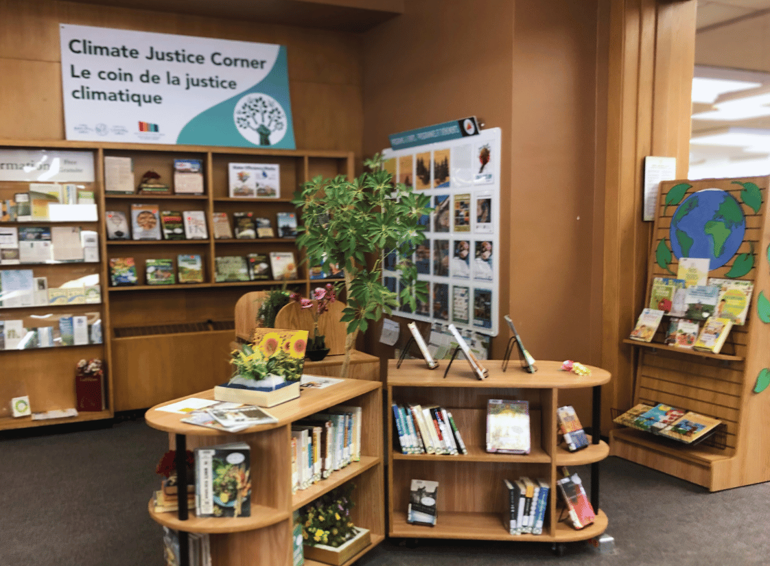 Climate Justice Corner Le coin de la justice climatique banner atop a bookshelf. Various bookshelves with books.