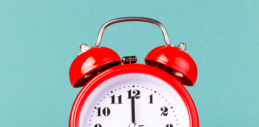 A red alarm clock with bells with the dial at 12:00 o'clock on a robin blue background.